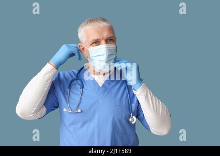 Medico maschile maturo che indossa maschera medica su sfondo blu Foto Stock