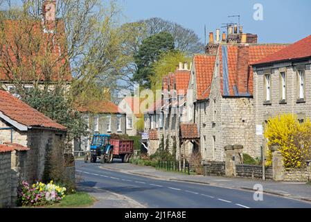 Trattore e rimorchio sulla strada B1257 attraverso il villaggio di Hovingham nel distretto di Ryedale, North Yorkshire, Inghilterra Regno Unito Foto Stock