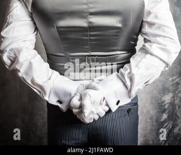 Primo piano di maggiordomo o cameriere in guanti bianchi in piedi con le mani dietro la schiena. Concetto di industria di servizio ed ospitalità elegante. Foto Stock