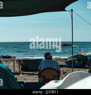 Vecchio pescatore in pensione guardando il mare seduto su una sedia di plastica a Malaga spiaggia, Spagna Foto Stock