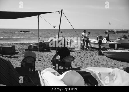 Due anziani pescatori in pensione che guardano un gruppo di giovani su una spiaggia a Malaga, Spagna Foto Stock