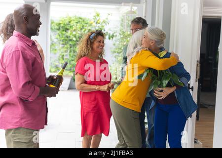 Donna anziana che accoglie gli amici multirazziali all'ingresso durante la festa della casa Foto Stock