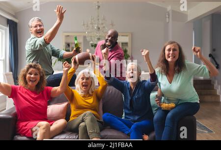 Multirazziale senior maschile e femminile amici che si acclamano mentre si guarda la partita di rugby in tv a casa Foto Stock