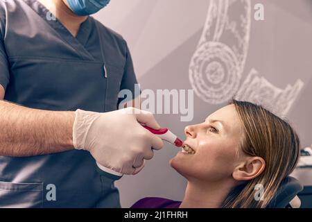 Dentista che seleziona il colore dei denti del paziente con comparatore digitale dei denti della guida dell'ombra Foto Stock