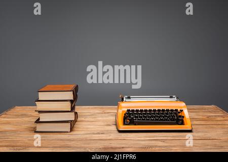 macchina da scrivere arancione e pila di libri su scrivania di legno isolato su grigio Foto Stock