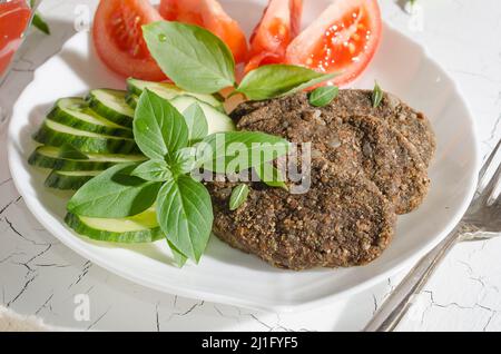 Cotoletta cruda di ortaggi e cereali con ortaggi e. erbe su un piatto bianco con luce dura Foto Stock