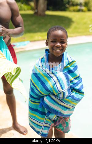 Ritratto di ragazzo afroamericano sorridente avvolto in asciugamano da padre a bordo piscina Foto Stock