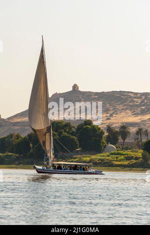 Felucca con Qubbet el-Hawa santuario in cima alla collina sulla riva occidentale del Nilo ad Assuan, Egitto Foto Stock
