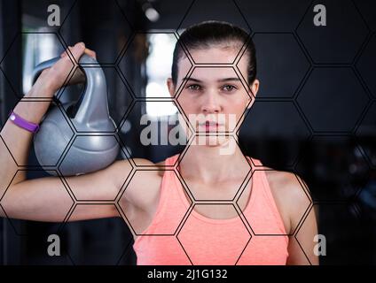 Modello esagonale contro ritratto di donna caucasica vestita tenendo un kettlebell in palestra Foto Stock