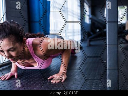 Forme esagonali modello contro caucasica fit donna esecuzione spingere in su esercizio in palestra Foto Stock