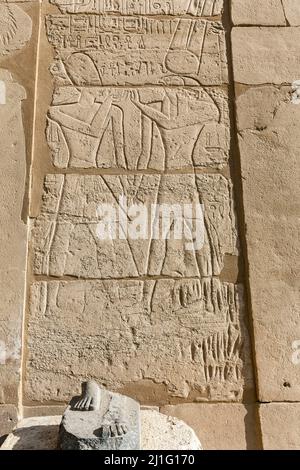 Rimasero i piedi dell'antica statua egizia, probabilmente Ramses II, a Karnak, con iscrizione sul muro dietro il faraone e il dio Amun Ra Foto Stock