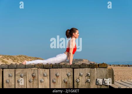 Giovane donna sportiva che si estende in Urdhva mukha shvanasana esercizio, rivolto verso l'alto cane posa. Ragazza sottile che pratica yoga all'aperto cielo blu. Foto Stock