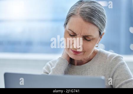 Devo fare il check-out. Shot di una donna d'affari matura seduta da sola in ufficio e soffrita di un collo irritato. Foto Stock