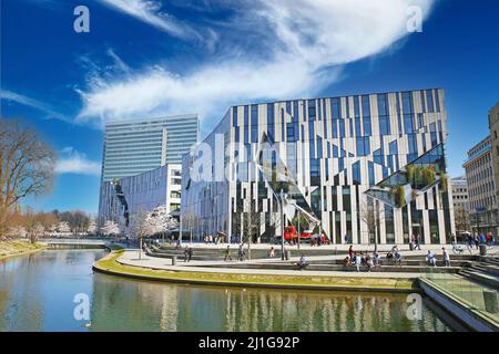 Düsseldorf, Germania - Marzo 23. 2022: Vista sullo stagno del parco sul futuristico Kö Bogen e sul grattacielo Dreischeibenhaus contro il cielo blu spettacolare, soffice Foto Stock