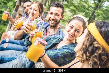 Amici felici bere sano succo di frutta d'arancia al pic-nic campagna - giovani millennial divertirsi insieme all'aperto per uno spuntino pomeridiano a. Foto Stock