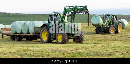 Trattore che carica balle di insilato sul rimorchio nella campagna irlandese Foto Stock