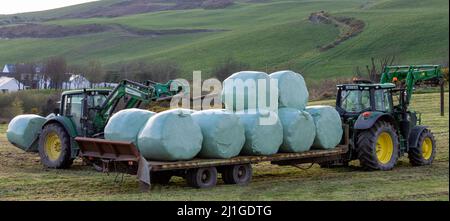 Trattore che carica balle di insilato sul rimorchio nella campagna irlandese Foto Stock