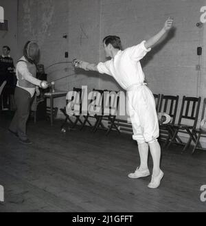 1960s, storico, classe di scherma, all'interno di una sala, uno studente maschile che indossa tradizionali breches scherma, praticando con un istruttore o insegnante di scherma, Università di Oxford, Inghilterra, Regno Unito. Stanno usando le epee, un'arma di thusting, un po'più pesante di un foglio, un'altra arma di scherma. L'istruttore indossa una maschera per il viso e una leggera giacca protettiva nota come zoppo. Uno sport di combattimento elegante ma foscialmente impegnativo, la scherma è uno dei soli cinque sport da avere in ogni moderno Giochi Olimpici. Foto Stock