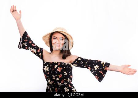 Ritratto di bella ragazza sorridente con capelli lunghi. La giovane donna indossa un abito floreale nero e un cappello e ha le braccia aperte. Foto Stock