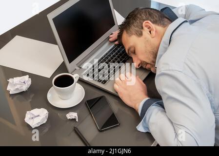 Uomo d'affari addormentato sul suo laptop, esausto da tutto il suo lavoro. Concetto di sovraccarico di lavoro Foto Stock
