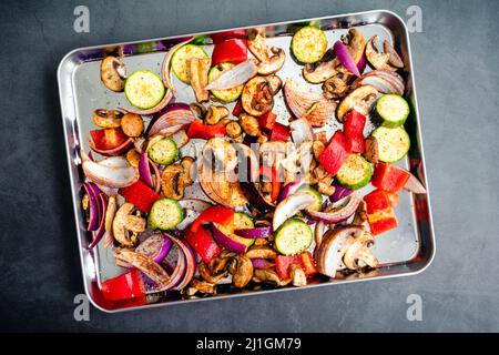 Vista dall'alto di verdure crude condite con olio d'oliva e spezie: Verdure affette e condite su una teglia Foto Stock