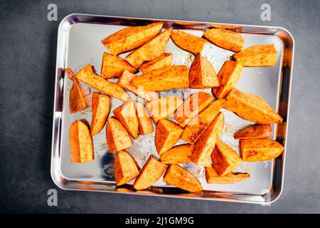 Spicchi di patate dolci crude su una teglie: Spicchi di patate dolci non cotte conditi con olio d'oliva, cumino e paprika affumicata Foto Stock
