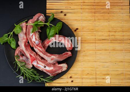 costolette di manzo con rosmarino e basilico su un piatto di ceramica nera, stuoia di bambù posto, e spazio vuoto per una ricetta Foto Stock