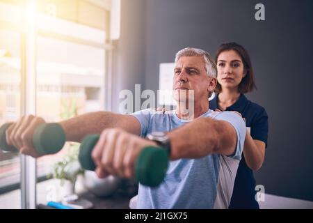 Devi mantenere la tua forza. Scatto corto di una giovane fisioterapista femminile che tratta un paziente maschio maturo. Foto Stock