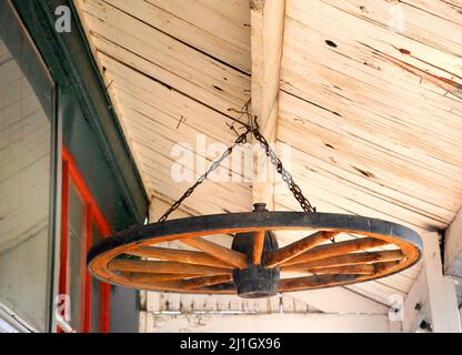 Vecchia ruota di legno del carro è riciclata ed usata come decorazione. È appeso nelle grondaie di una vecchia casa nel Wyoming. Foto Stock