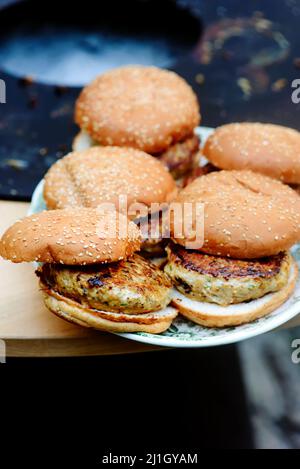 Hamburger di pollo che cucinano su una griglia all'aperto. Fuoco selettivo Foto Stock