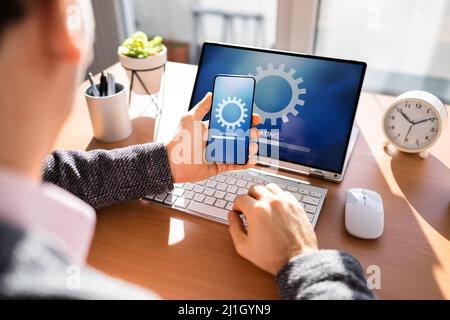 Man che esegue l'aggiornamento del software su telefono cellulare e laptop Foto Stock