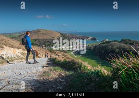 Ragazza con cappuccio blu e con lo zaino nero guarda sulla Lulworth Cove, Jurassic Coast, Dorset, UK Foto Stock