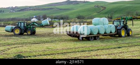 Trattore che carica balle di insilato sul rimorchio nella campagna irlandese Foto Stock
