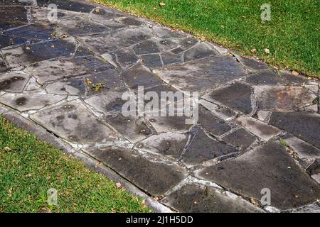 un percorso in pietra giardino fatto di ciottoli di varie forme lastricato in un sentiero bagnato dopo la pioggia circondato da un prato verde, un primo piano del parco paesaggistico Foto Stock