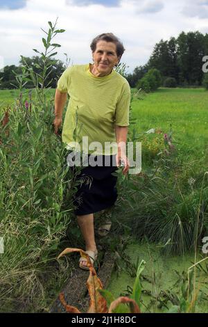 Polesie, Polesia, Polesien, Polska, Polen, La Polonia, una donna anziana attraversa la passerella su una fossa piena d'acqua. Foto Stock