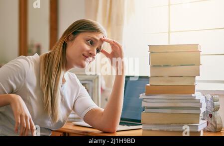 Questo è ciò che ottengo per procrastinating. Girato di una giovane donna che guarda sopraffatta dal mucchio di libri sulla sua scrivania. Foto Stock