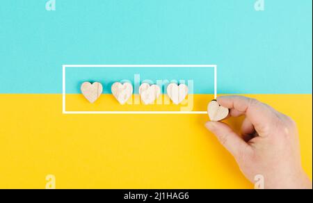 Cinque cuori su uno sfondo blu e giallo, mano mettere l'ultimo cuore in fila, valutare, dare feedback, valutazione aziendale Foto Stock
