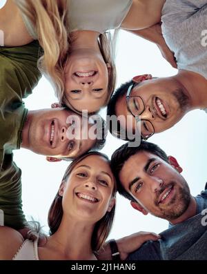Mettere insieme la testa. Ritratto ad angolo basso di un giovane gruppo di amici in piedi fuori in un huddle. Foto Stock