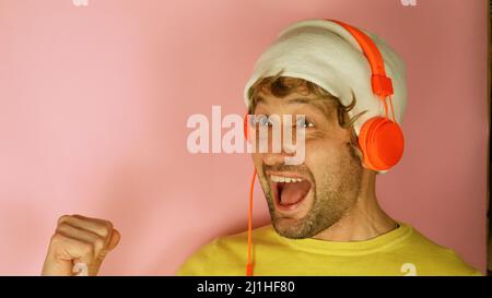 Giovane uomo indossare cuffie giallo camicia ascoltare musica cantare voce record isolato su semplice pastello rosa sfondo ritratto studio. Foto Stock