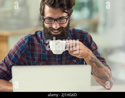 Trova l'ispirazione che ti serve per avere successo. Scatto di un designer che ha un caffè mentre lavora sul suo laptop. Foto Stock