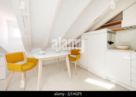 tavolo da pranzo accanto alla cucina bianca con ripiani in legno in appartamento mansarda Foto Stock