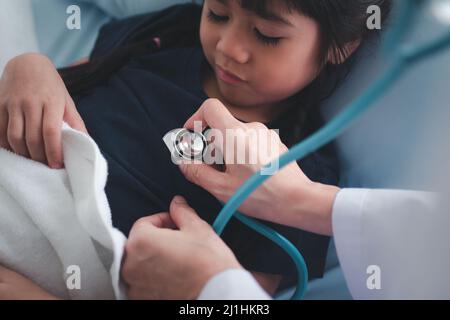 Donna asiatica medico pediatra tenere stetoscopio per l'esame una piccola ragazza paziente e heck cuore polmoni di bambino, buon medico di famiglia in visita bambino a casa Foto Stock