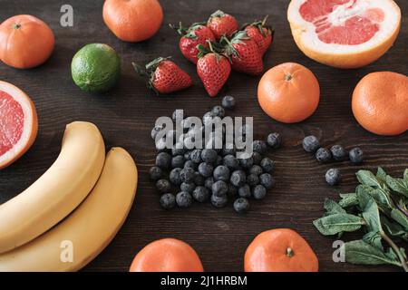 Primo piano di frutta e frutti di bosco colorati e brillanti su tavola di legno scuro, ingredienti per frullati Foto Stock