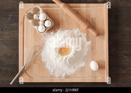 Direttamente sopra la vista di legno con farina, uova, whisk e spina di rotolamento sul banco della cucina Foto Stock