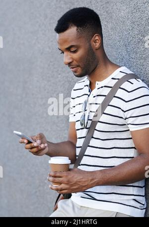 Organizzazione di una riunione. Un bel uomo d'affari afroamericano appoggiato contro un muro della città mentre usa il suo cellulare. Foto Stock