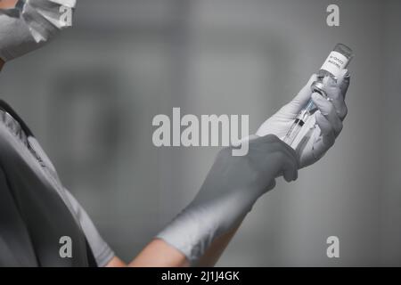 Primo piano di un operatore medico non riconoscibile che indossa dispositivi di protezione individuale siringa di riempimento con vaccino Covid-19, spazio di copia Foto Stock