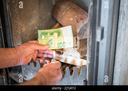 Vecchio uomo pensionato che tiene le banconote in mano di fronte alla stufa a legna e che brucia l'accendino in un appartamento, la Germania Foto Stock