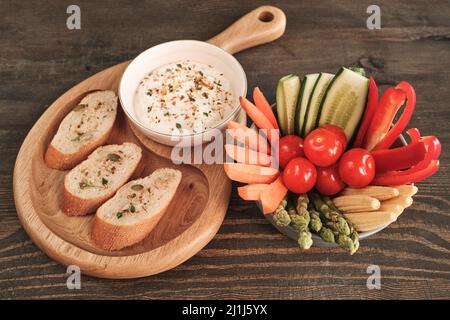 Sopra la vista di snack sani come fette di verdure mature e toast baguette con salsa piccante su tavola di legno Foto Stock