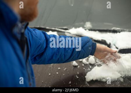 Rimozione della neve dall'auto. La mano raschia il ghiaccio dall'automobile. L'uomo rimuove la neve. Foto Stock