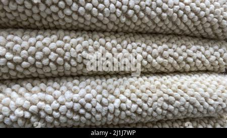 Una pila di moquette piegata. La tessitura del tappeto per la casa è fatta di materiale naturale. Colore naturale della biancheria Foto Stock